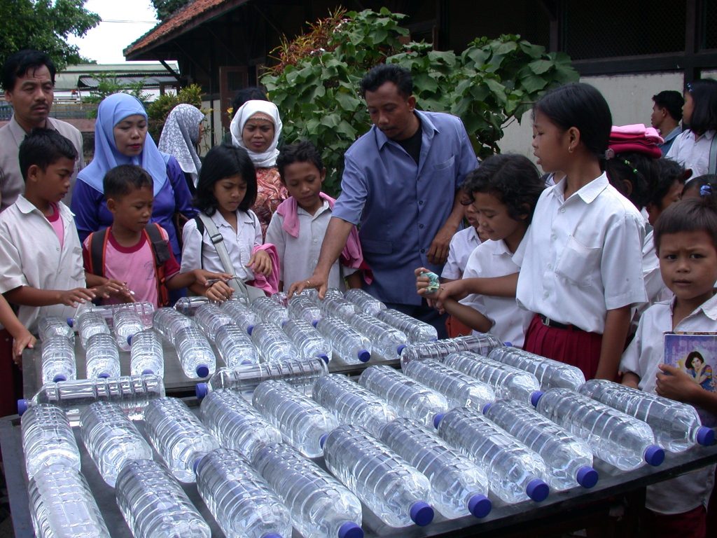 A group of people surround rows of filled water bottles in a village