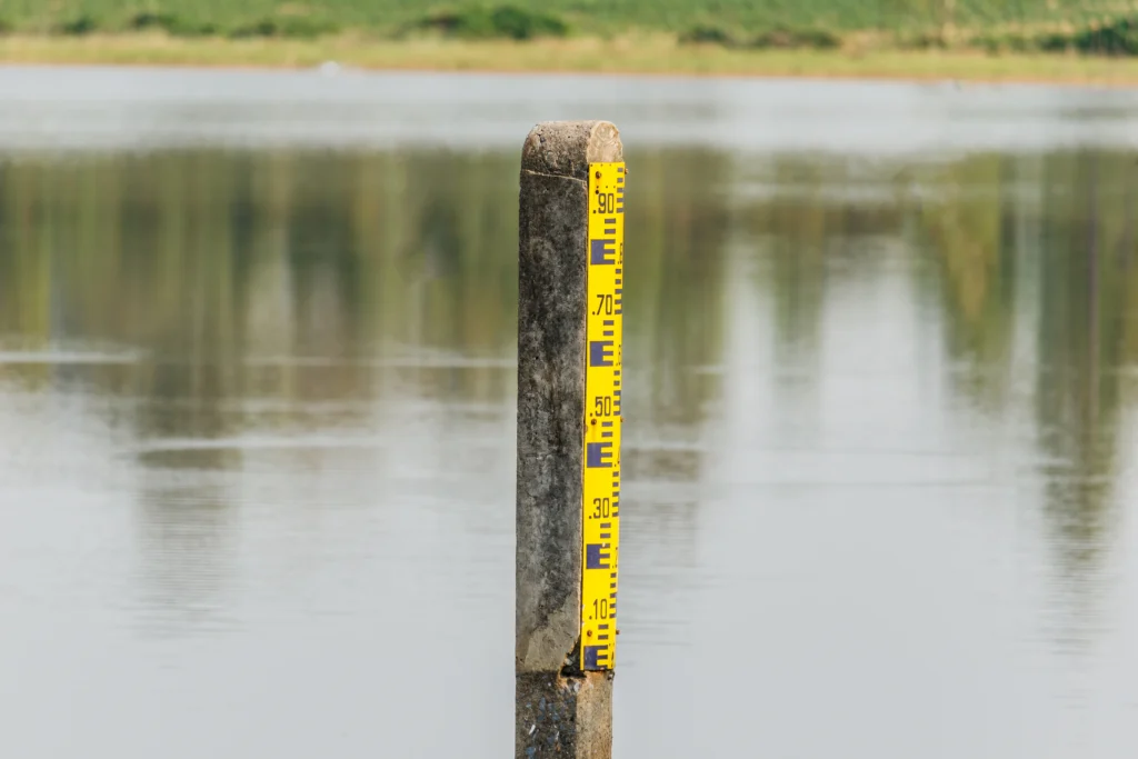 A yellow water level marker standing in a calm waterway with a grassy shoreline in the background.