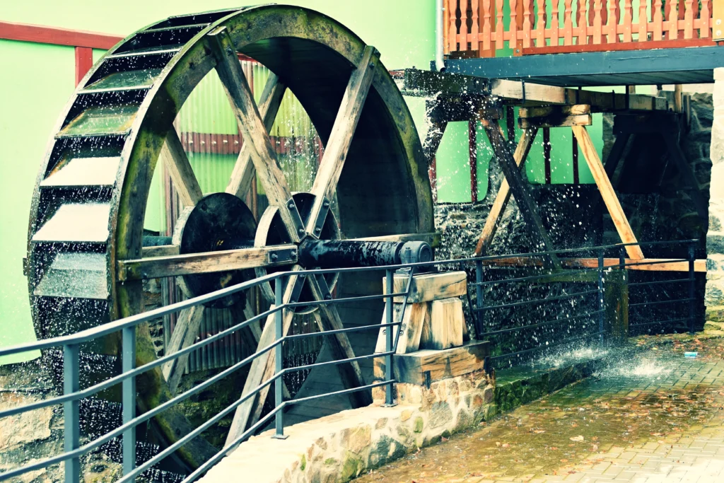A close-up of a wooden watermill with water splashing onto its spinning wheel in a rustic setting.