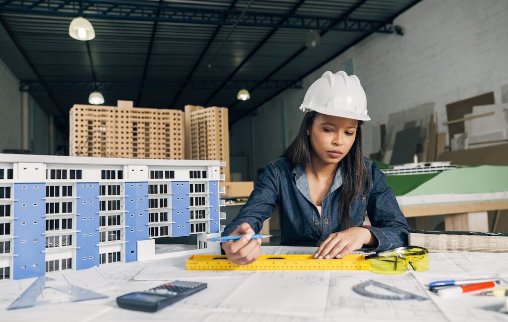A woman sitting at a drafting table with a model in the background. 