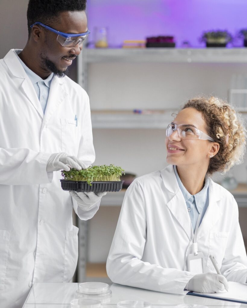 A man holding a tray of plants while a woman in safety glasses writes on a clipboard
