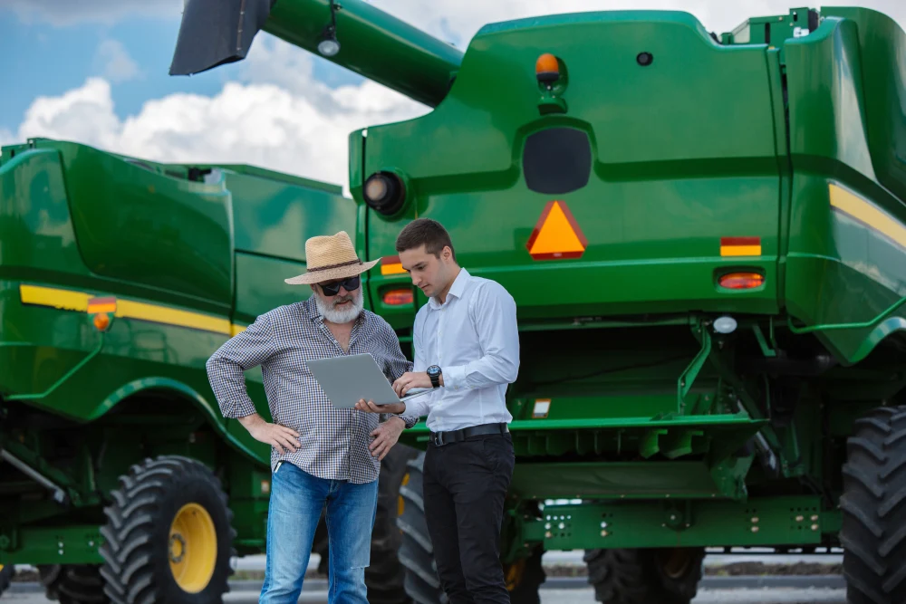Two men looking at a laptop in front of new farming equipment.