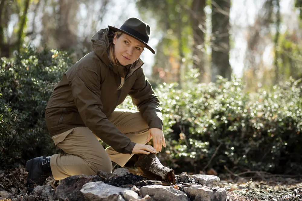 A park ranger squatting near a burnt out fire pit and checking the surrounding area.