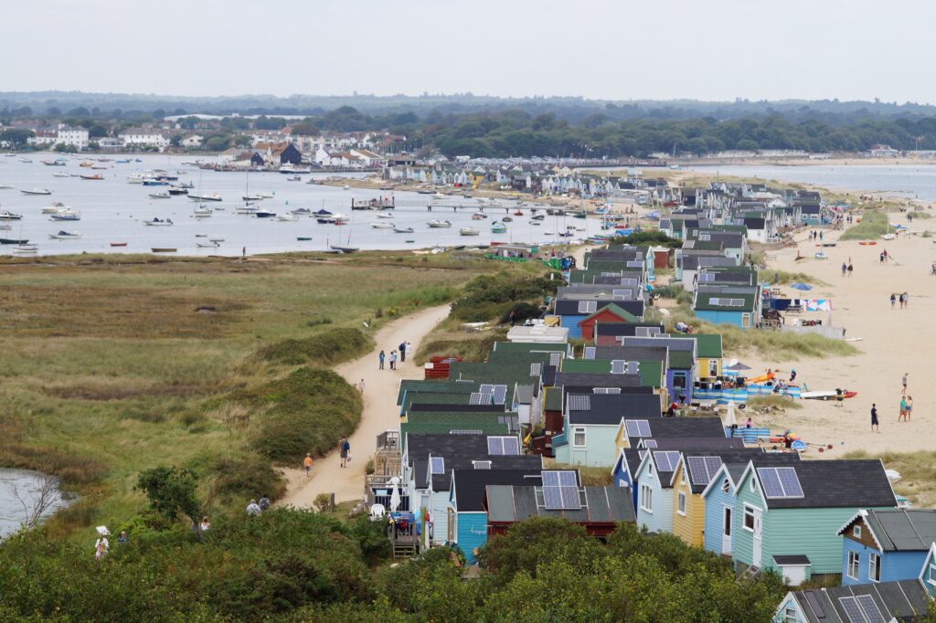 A scenic high-angle view of a coastal town with colorful houses, a sandy beach, and boats moored in the water. The area shows human settlement and interaction with the marine environment.