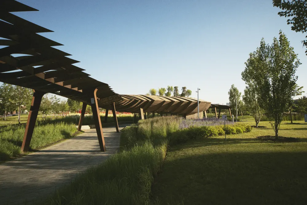 A modern sun shade structure covers a path in a park.