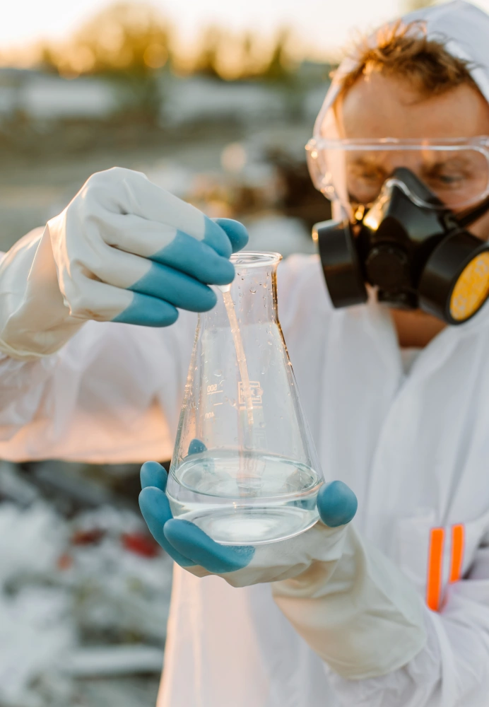 Ecologist in safety equipment tests a sample in a beaker.