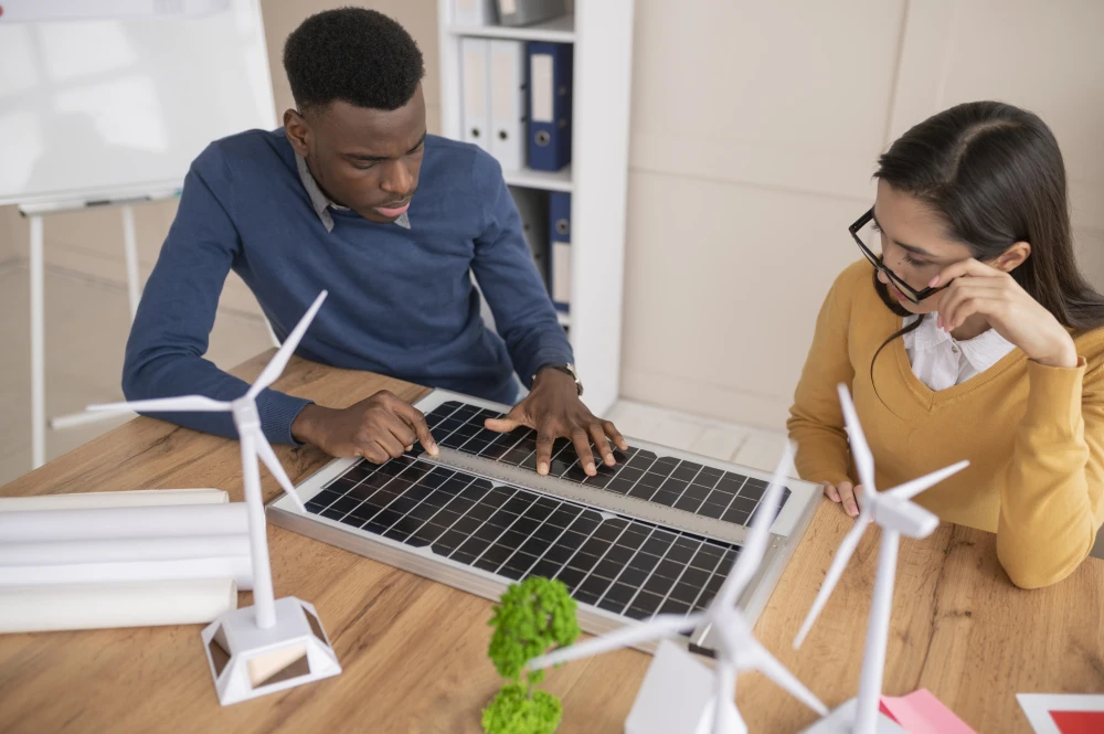Two engineers working on renewable energy solutions by measuring a desktop solar panel.