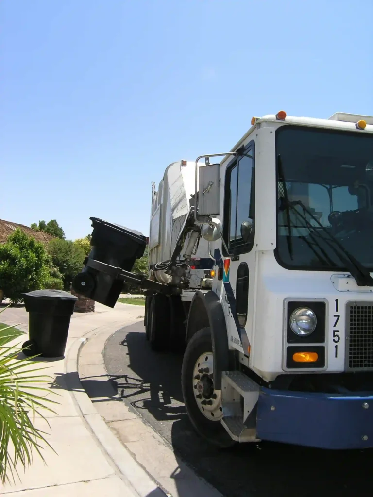 A garbage truck is lifting a large bin about halfway up the side of the truck with a mechanical grabbing arm to lift over the top and dump the contents of the bin.