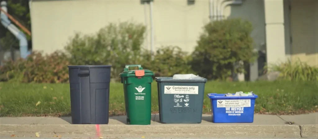 4 bins on the curb. A garbage bin, a green compost bin, a containers only bin, and a blue paper and plastics bin.