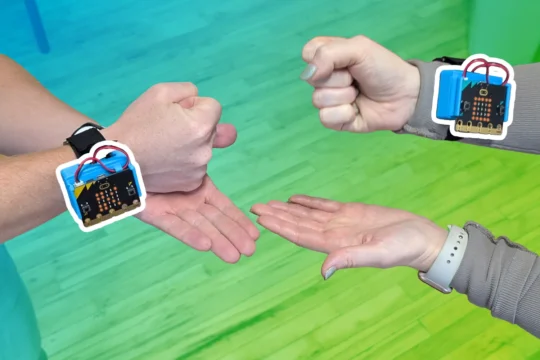 Two people's hands playing Rock Paper Scissors with CHARGE power packs and micro:bits attached to their wrists. A blue to green gradient is overlaid behind the micro:bit which has a white boarder around it.