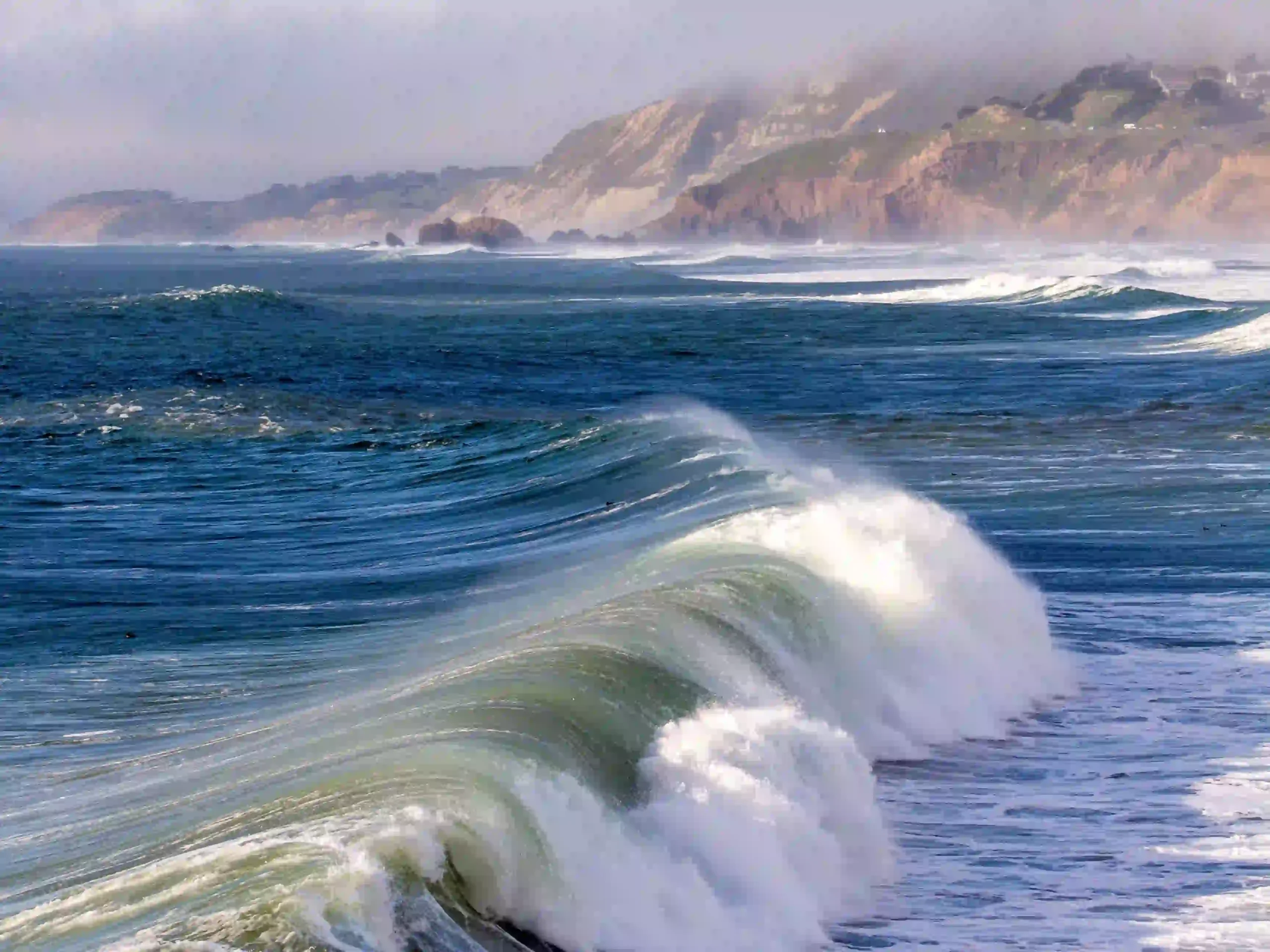 Rolling waves along a beach with rocky cliffs in the distance