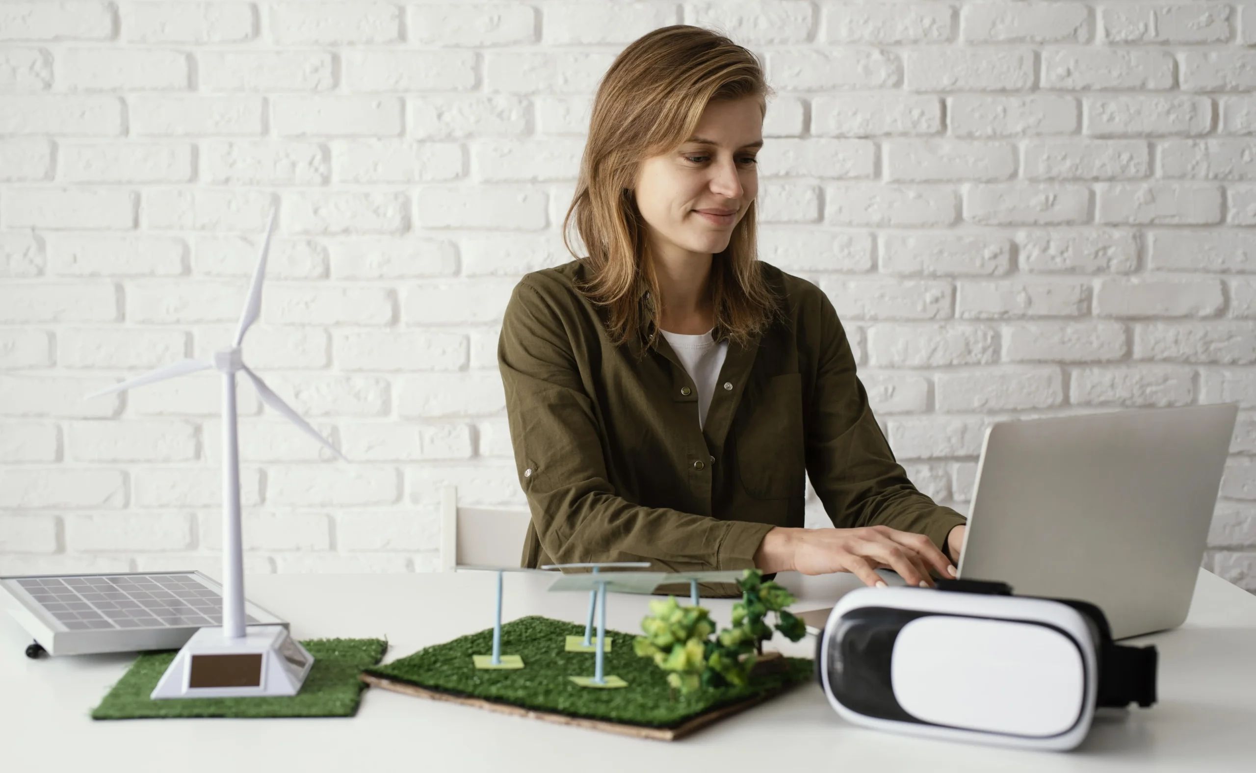 A woman sitting at a desk using a computer surrounded by models of wind turbines and sustainable energy