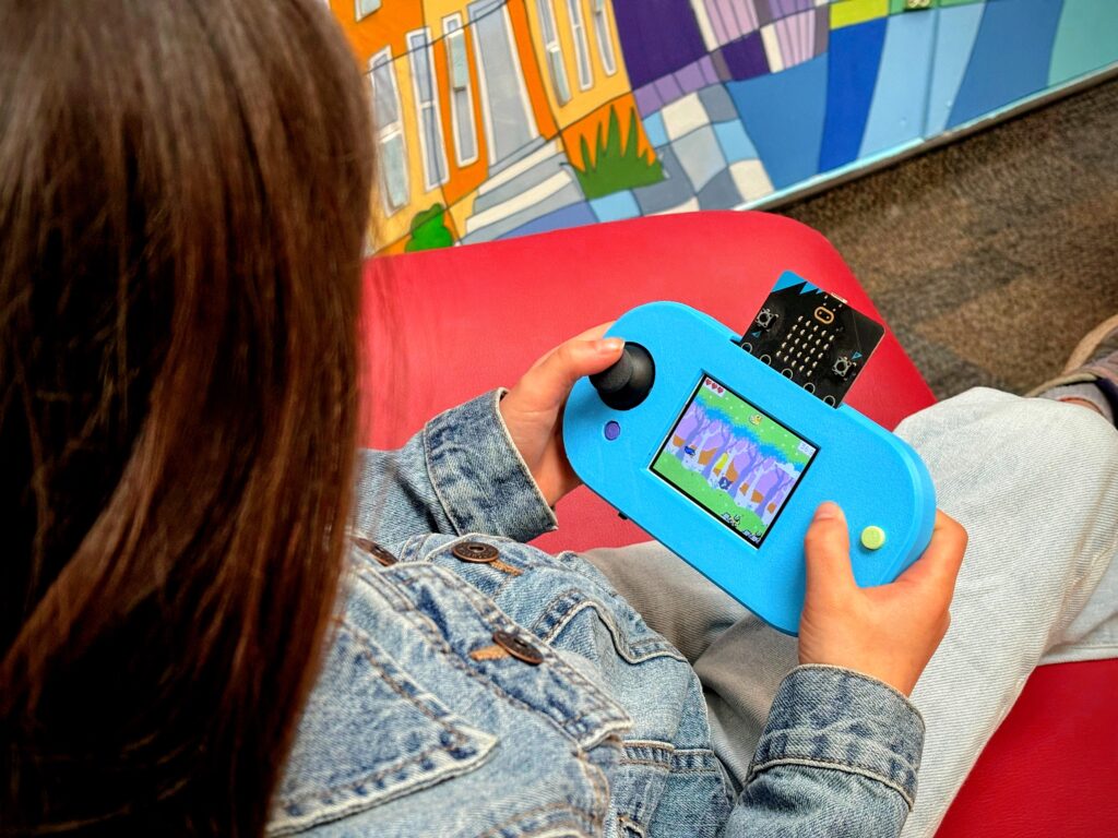 A child uses Forward Education's CodeCTRL device to play a colorful pixel-art video game.
