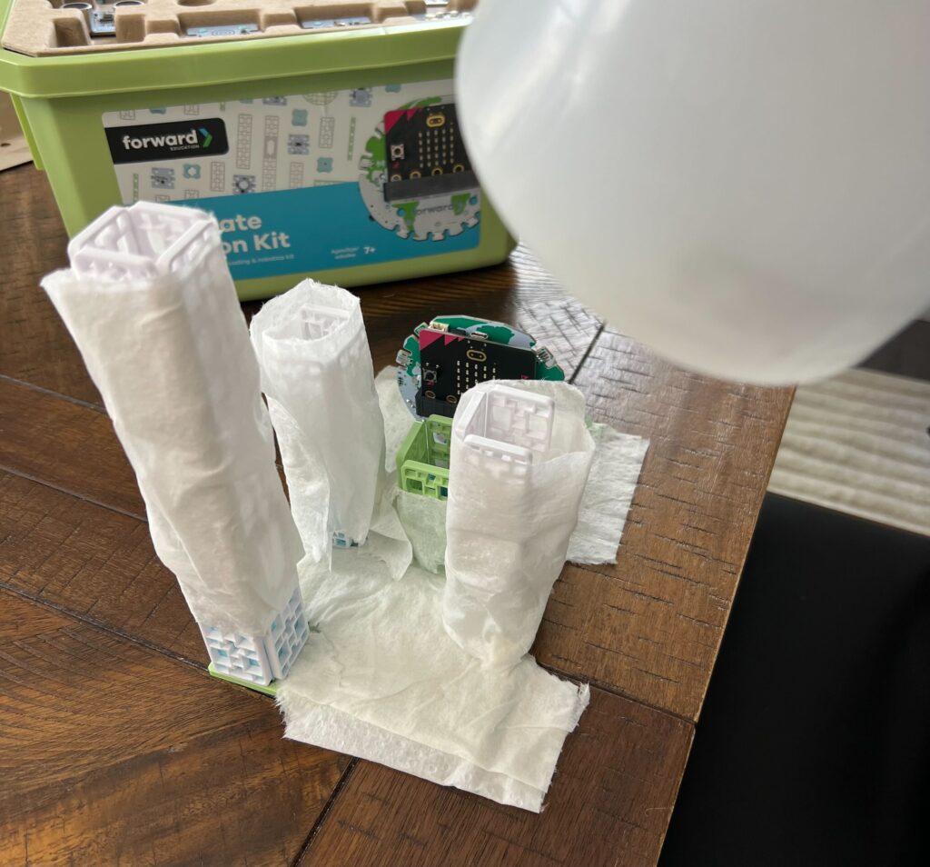 Base model city build plus damp, white paper towel coverings for Eliminating Urban Heat Islands experiment. Incandescent lamp acts as a heat/light source above the model.