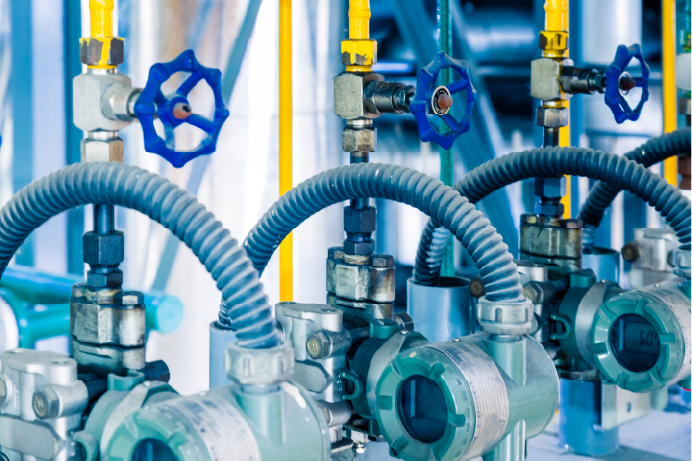 A close-up view shows a series of industrial pipes with blue valves and pressure gauges.