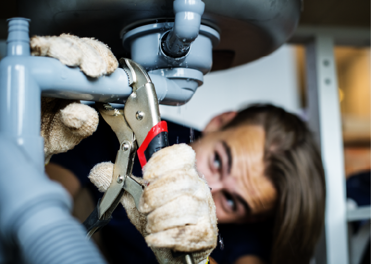 A person holding a pipe wrench tightening a pipe.