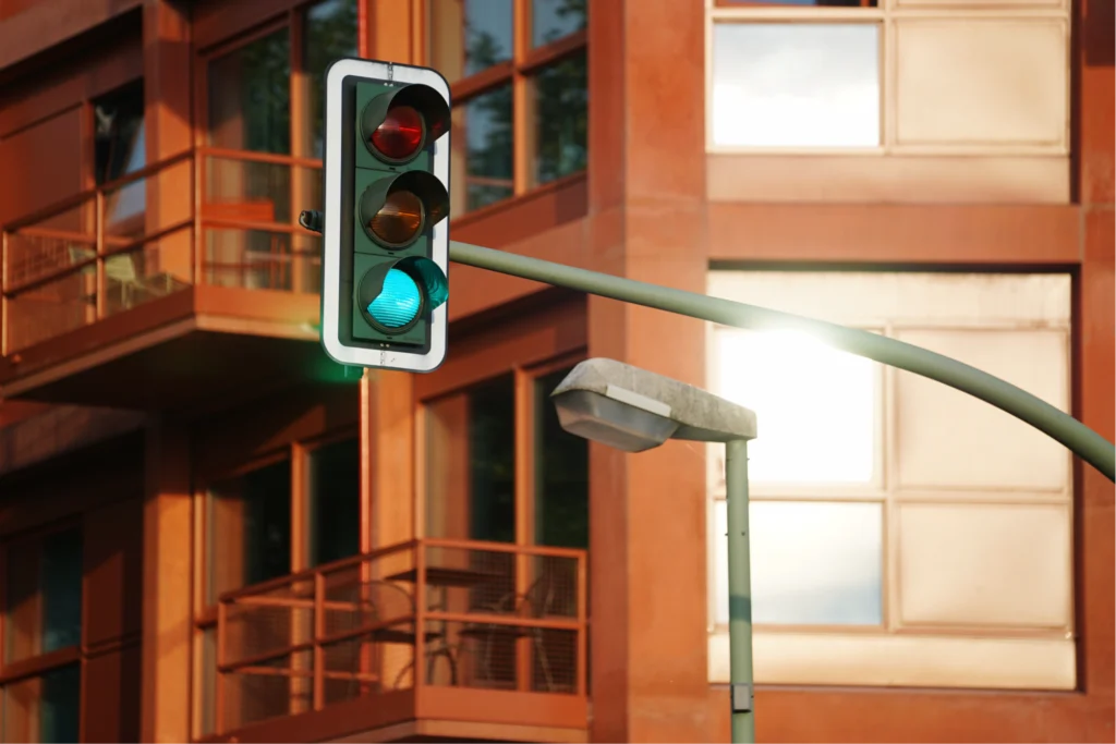 A modern traffic light displays a green signal against the backdrop of a building with warm orange tones and large windows.