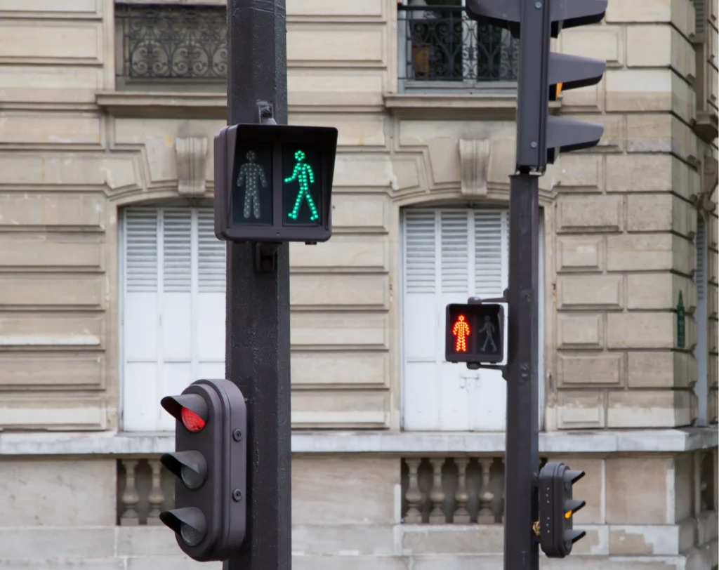 Two pedestrian traffic signals are mounted on a dark pole, with one showing a green "walk" symbol and another a red "don't walk" symbol, set against a classic building facade.
