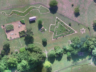 An aerial photograph shows a large garden with plots and pathways designed in culturally significant shapes, including a large arrowhead and a long, winding snake.