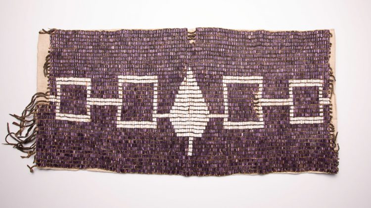 The Hiawatha Wampum Belt shows five connected white symbols—a central tree and four squares—on a background of purple beads, representing the unity of the five nations of the Haudenosaunee Confederacy.