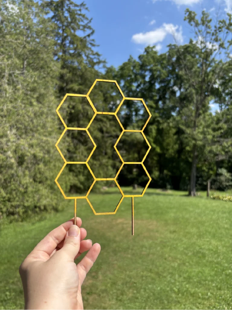 A hand holding a honeycomb patterned plant trellis painted yellow for use in a plant pot