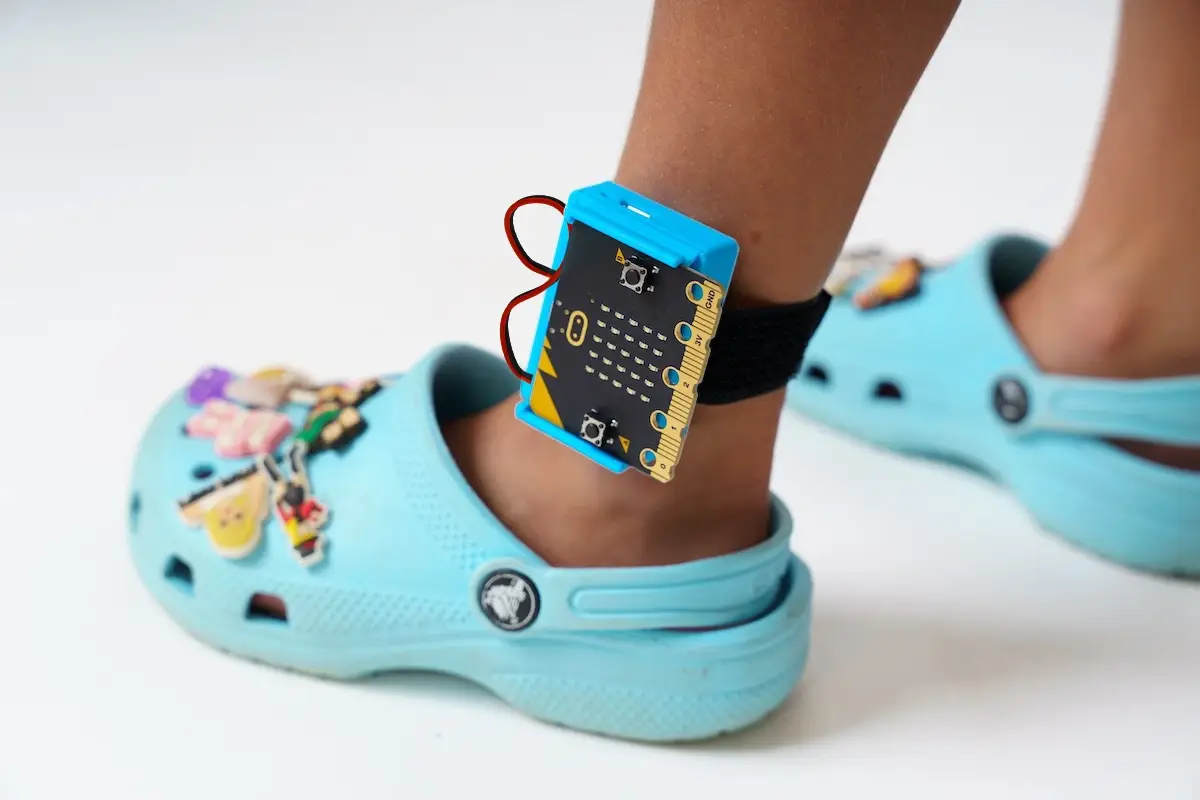 Closeup of a Charge for micro:bit wrapped around a child's ankle wearing crocs.